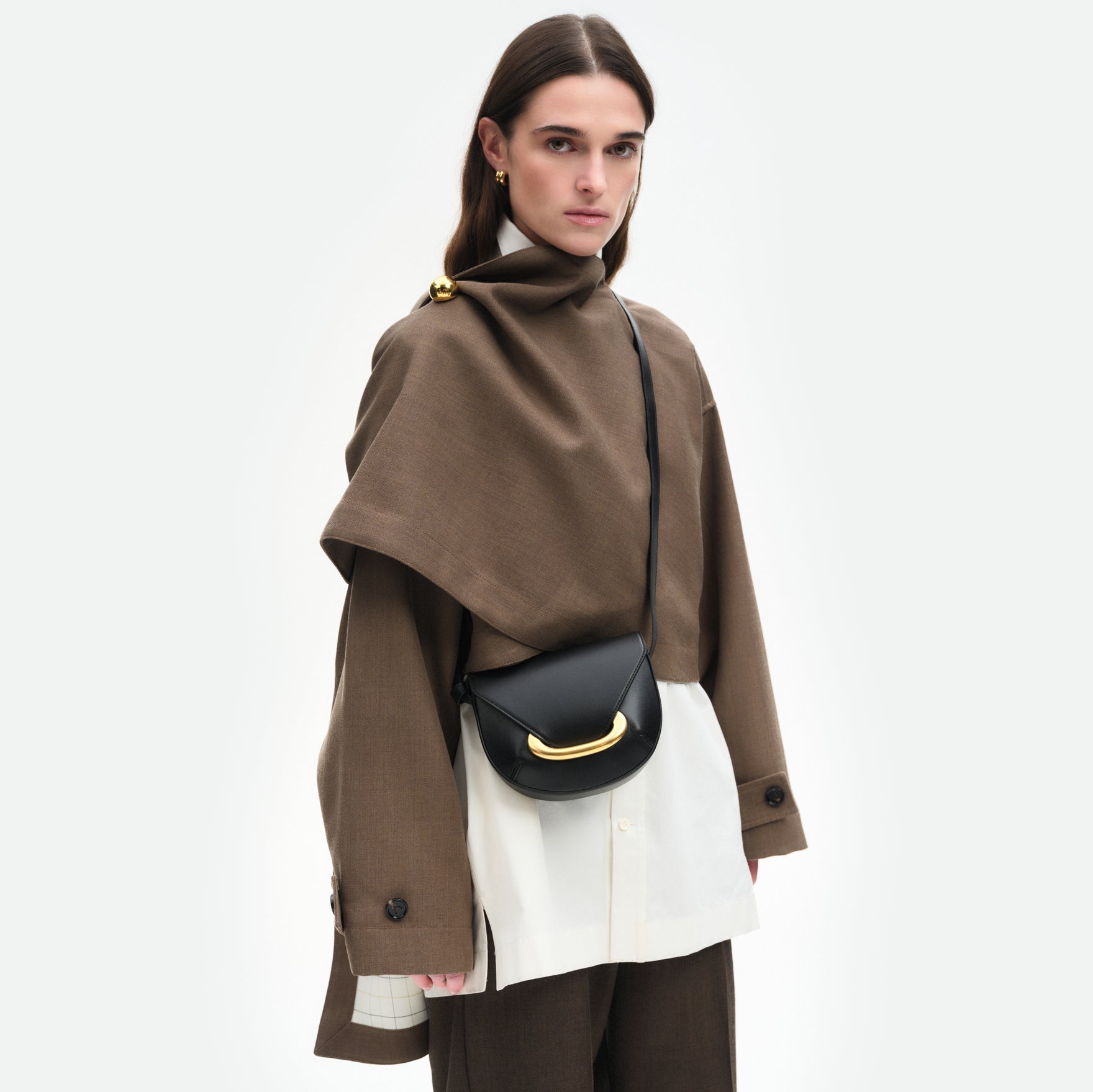 Wandler Veneto Crossbody Small in Black, made from Italian calf leather with golden clasp hardware and structured silhouette, pictured on model, worn in a crossbody style, half body picture. 