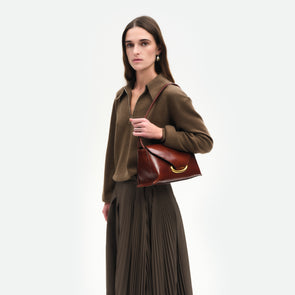 Wandler Veneto Shoulder Bag in the color in Palissander Glaze, deep dark red, Italian calf leather with oversized golden clasp hardware and structured silhouette, shown on model, worn on the shoulder. 