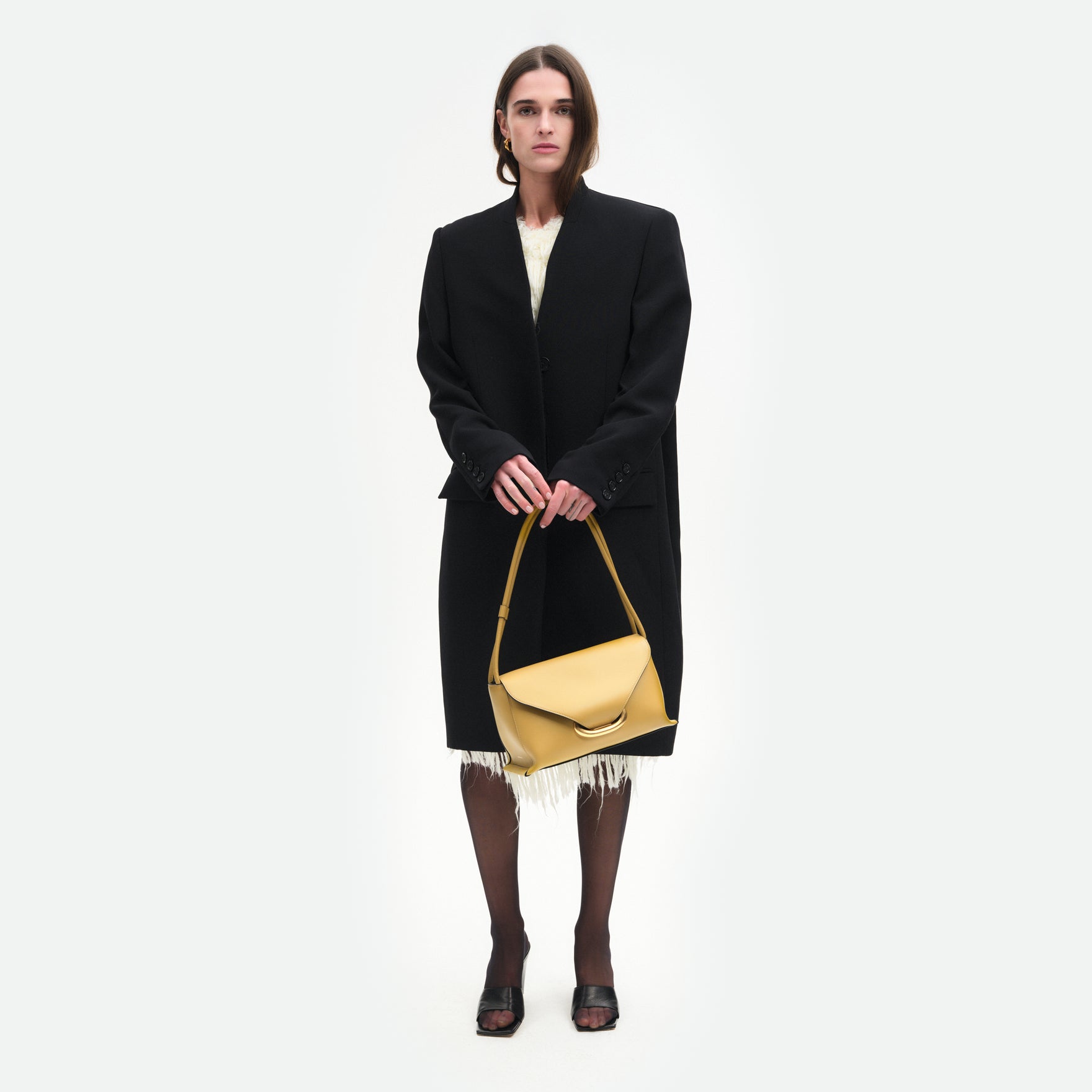Wandler Veneto Shoulder Bag in the color Saffron, yellow, Italian calf leather with oversized golden clasp hardware and structured silhouette, handheld by the model.