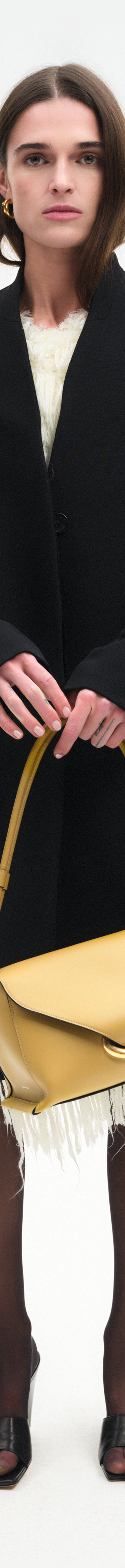 Wandler Veneto Shoulder Bag in the color Saffron, yellow, Italian calf leather with oversized golden clasp hardware and structured silhouette, handheld by the model.