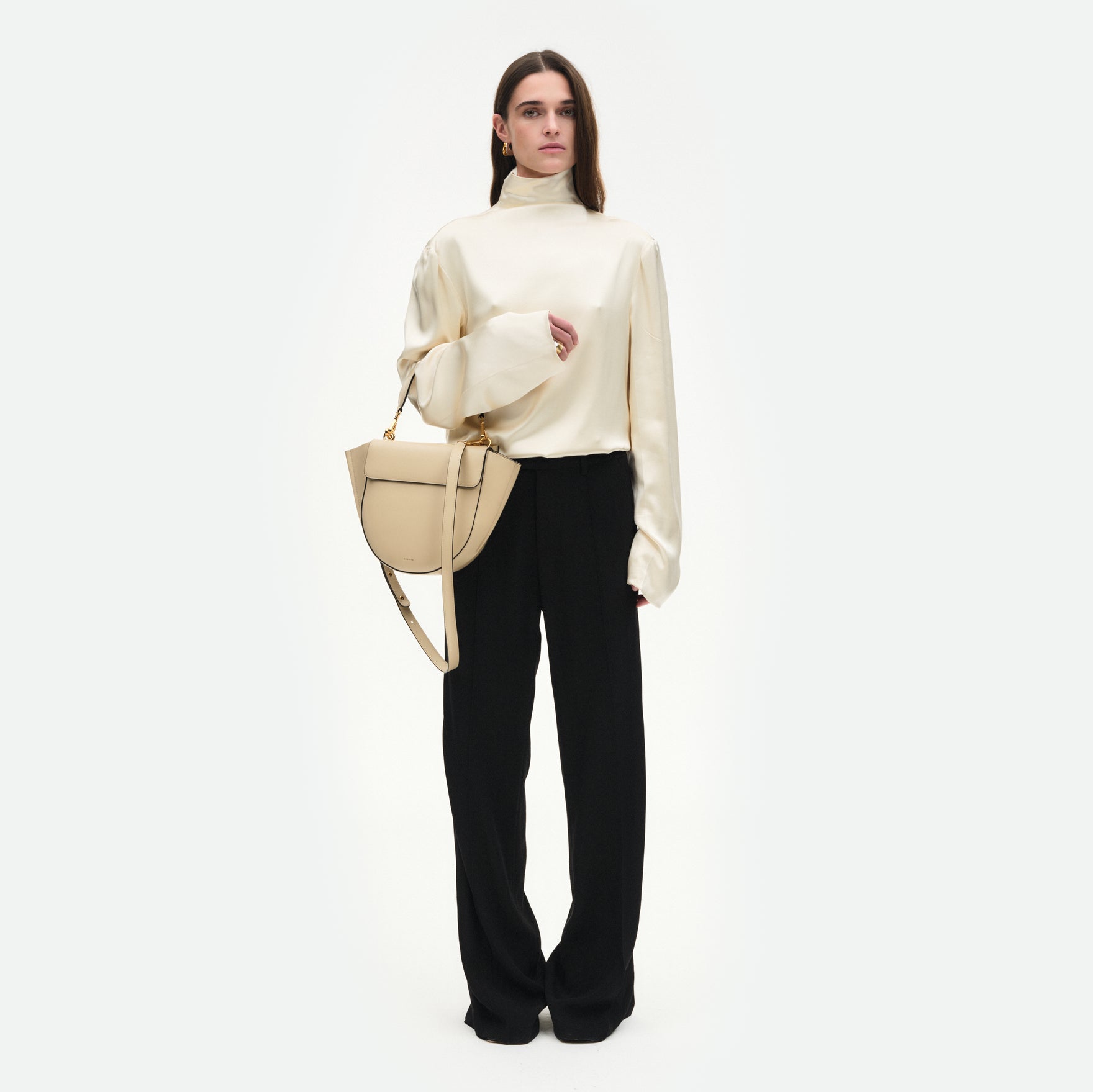Wandler Hortensia Bag Medium  in the color Linen, beige, made from Italian calf leather with golden hardware, rounded silhouette and top handle, pictured on model, worn on the forearm, full body picture. 