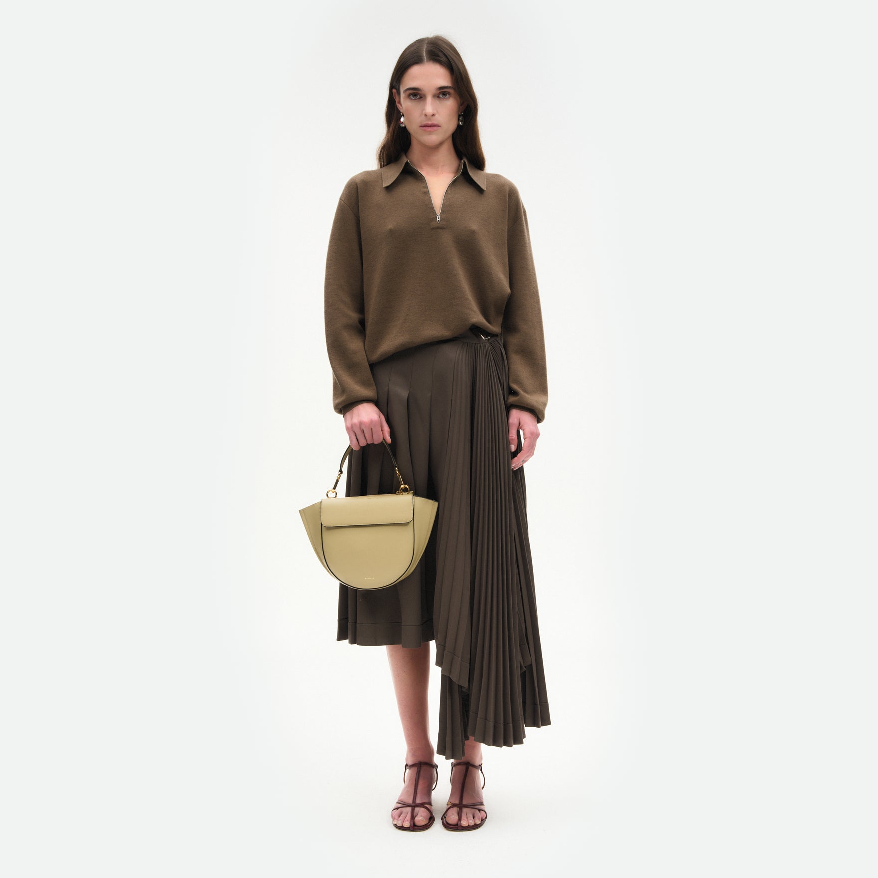 Wandler Hortensia Bag Small in the color Peper, dark beige, Italian calf leather with golden hardware and rounded silhouette, front view. Pictured being hand-held by model. 
 