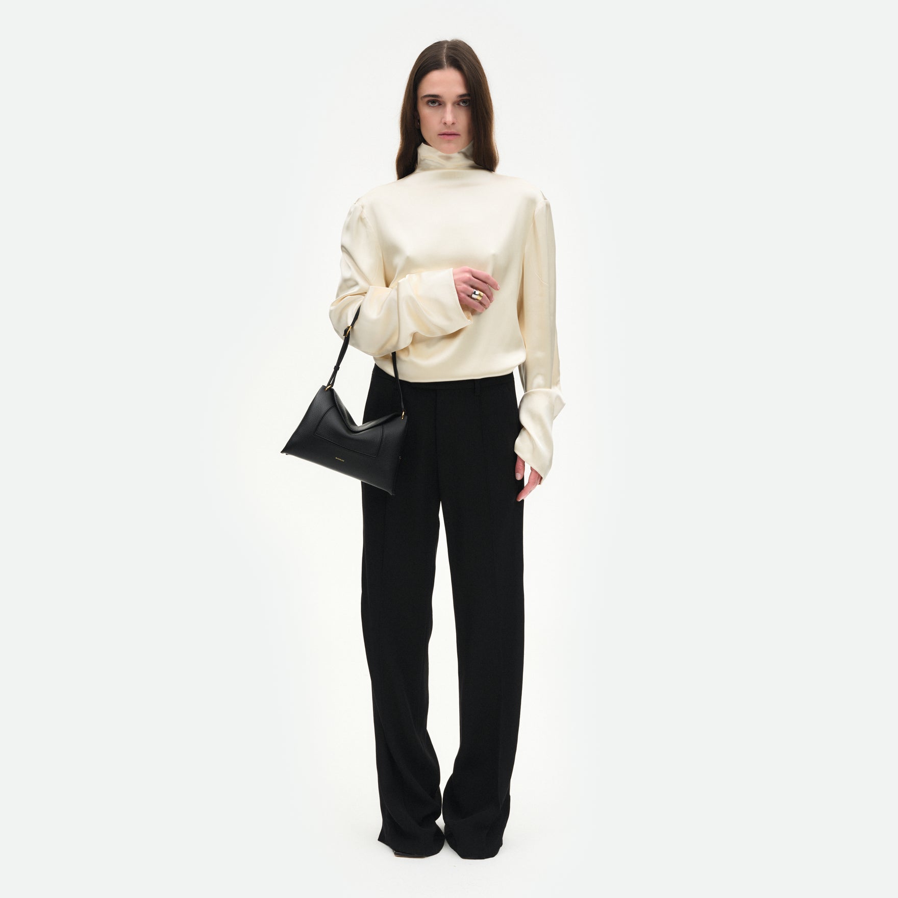 Wandler Penelope Slouch Bag in the color Black Crust, made from smooth calf leather with golden hardware and adjustable slim strap, pictured on model being worn on the forearm, full body view. 