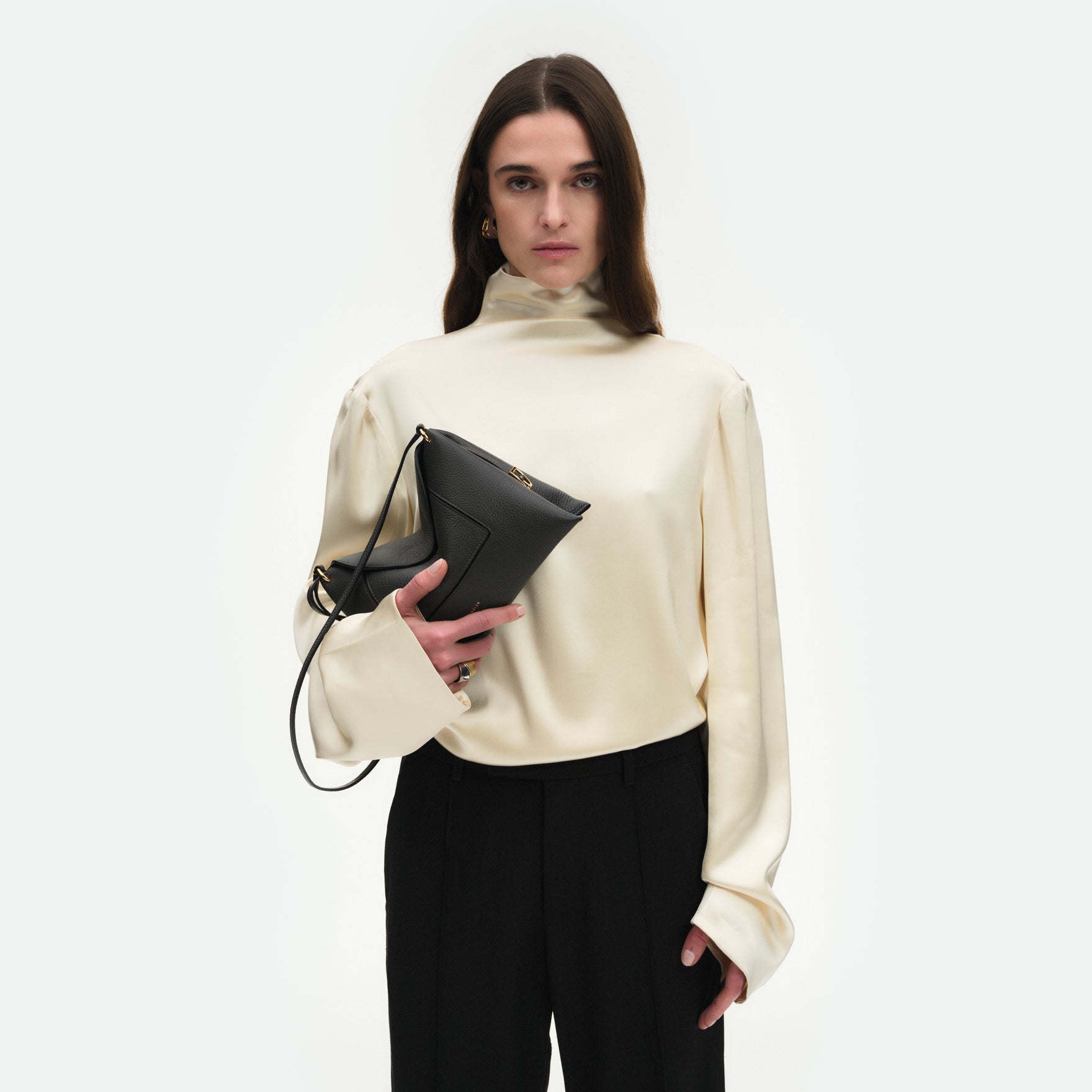 Wandler Penelope Slouch Bag in the colour Space Crust, grey, made from smooth calf leather with golden hardware and adjustable slim strap, pictured being held in the hand by model, half body picture.