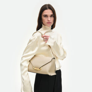 Wandler Veneto Shoulder Bag in the color Linen, beige, Italian calf leather with oversized golden clasp hardware and structured silhouette, worn by model in the cross body style 