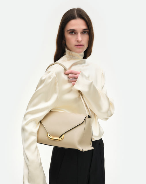 Wandler Veneto Shoulder Bag in the color Linen, beige, Italian calf leather with oversized golden clasp hardware and structured silhouette, worn by model in the cross body style 