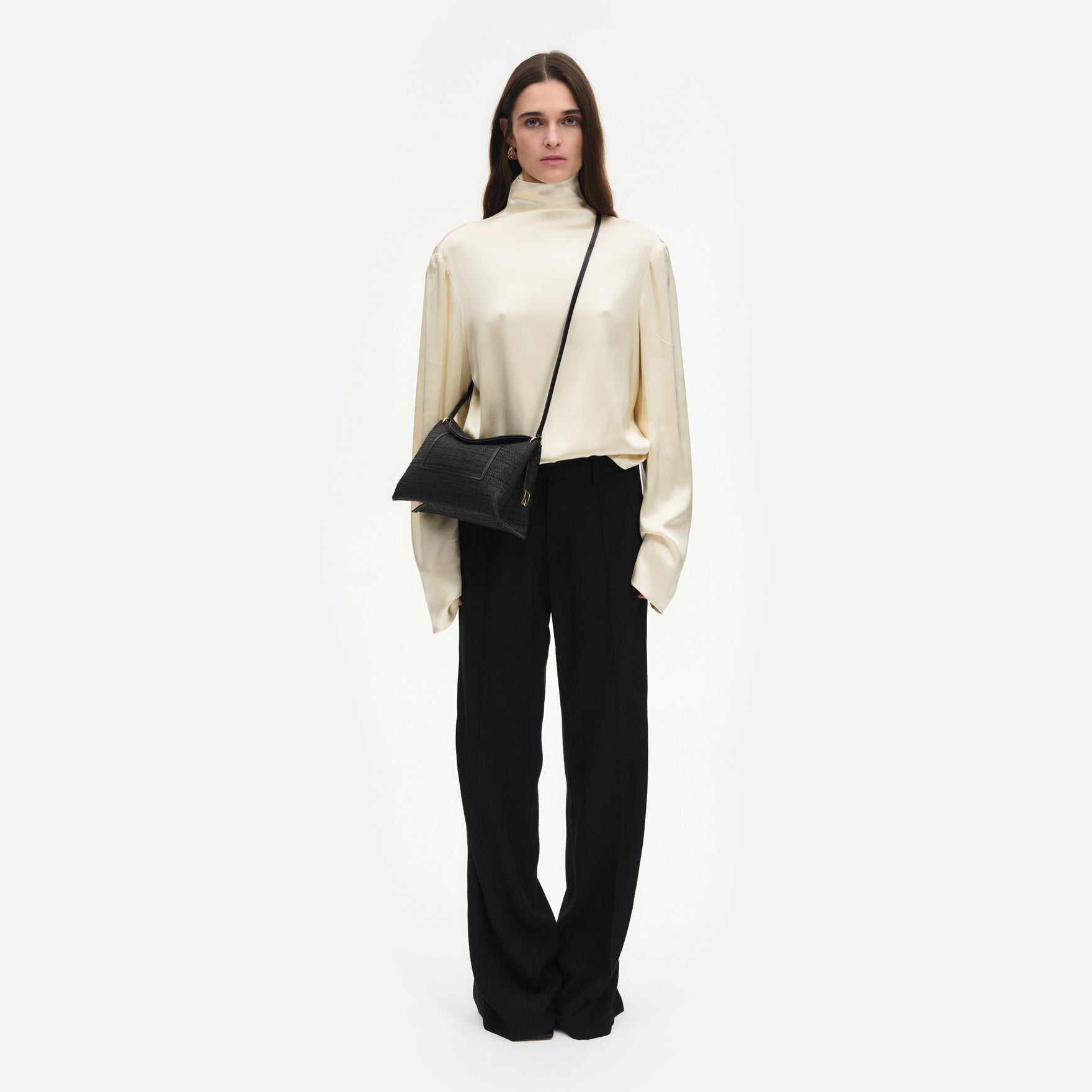 Wandler Penelope Slouch Bag in the color Black Raffia, made from raffia and smooth calf leather with golden hardware and adjustable slim strap, pictured on model worn in a crossbody style. 