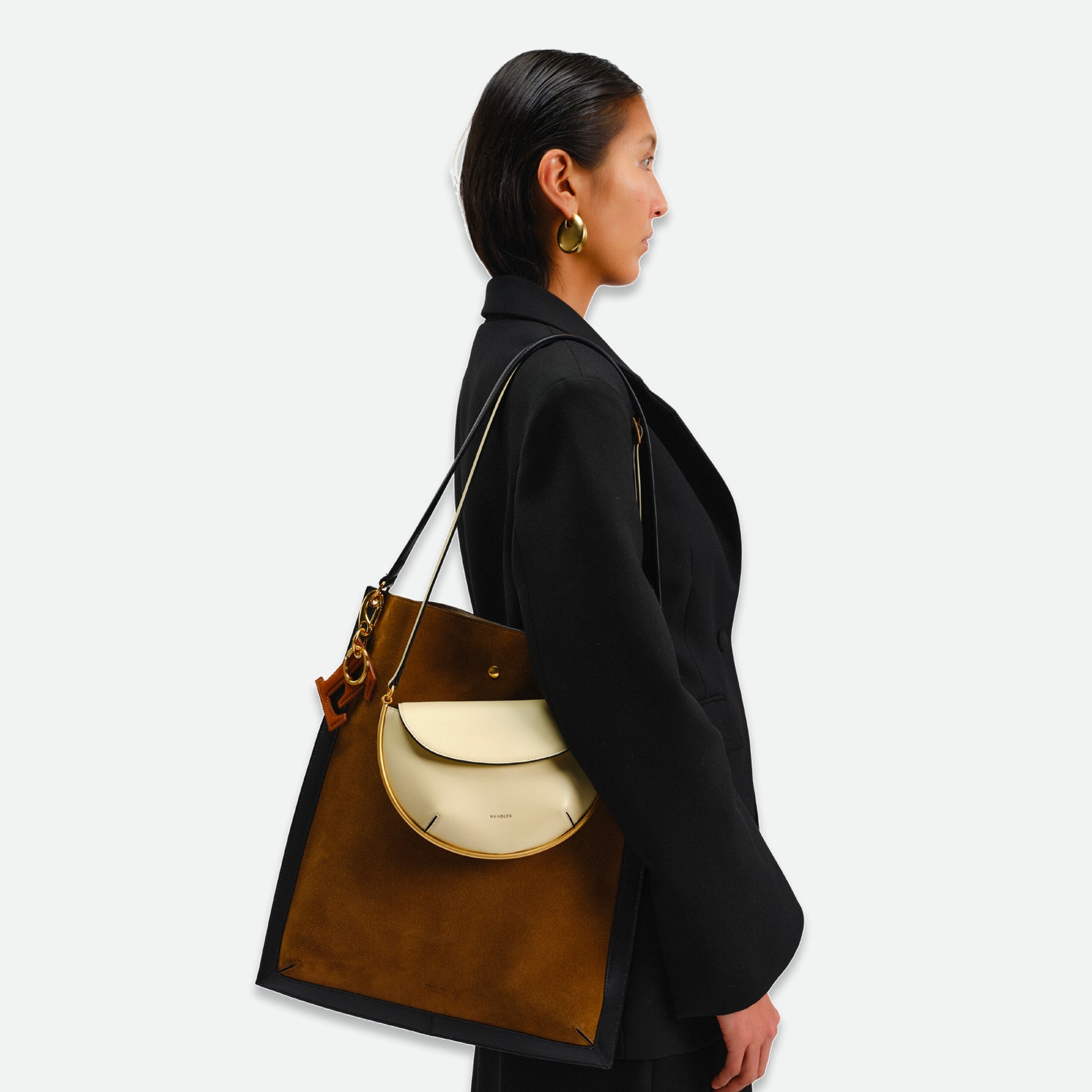 Wandler Penny Tote in the color Tabacco Suede, made from Italian calf leather with hand-painted black edges and golden hardware, being worn on the shoulder by model together with other bag.