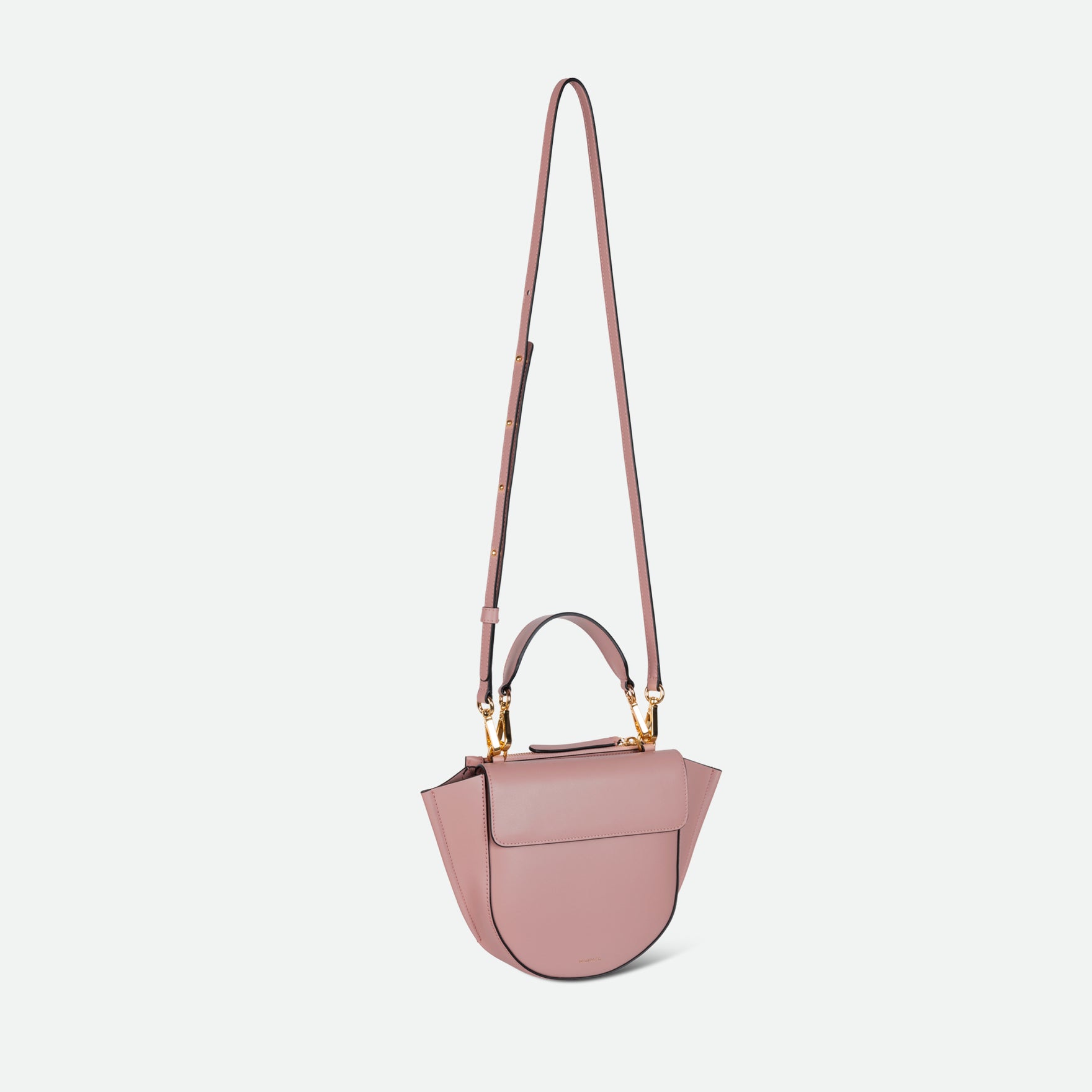 Wandler Hortensia Bag Mini in the color Apricot, light pink, Italian calf leather with golden hardware, rounded silhouette and top handle. The bag is pictured with the crossbody strap extended into the air.