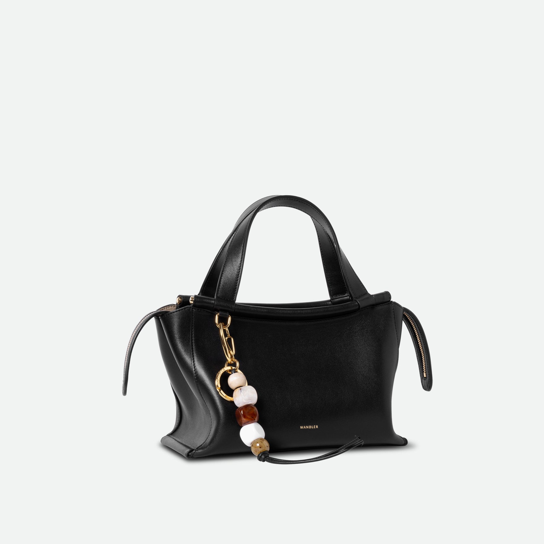 Wandler Ida Bag in the color Black, made from Italian calf leather with golden hardware and sculptural top handle, pictured with bag charm attached.