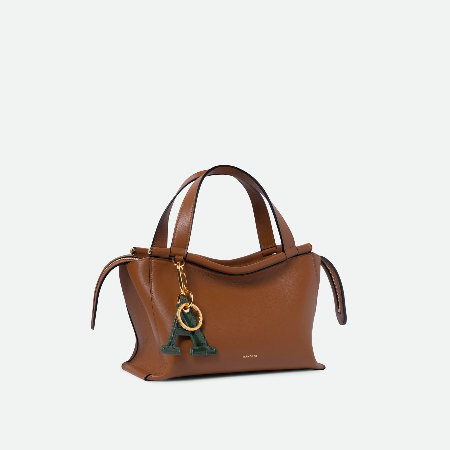 Wandler Ida Bag in the color Saddle, warm brown, made from Italian calf leather with golden hardware and sculptural top handle, pictured with a bag charm attached to the bag. 