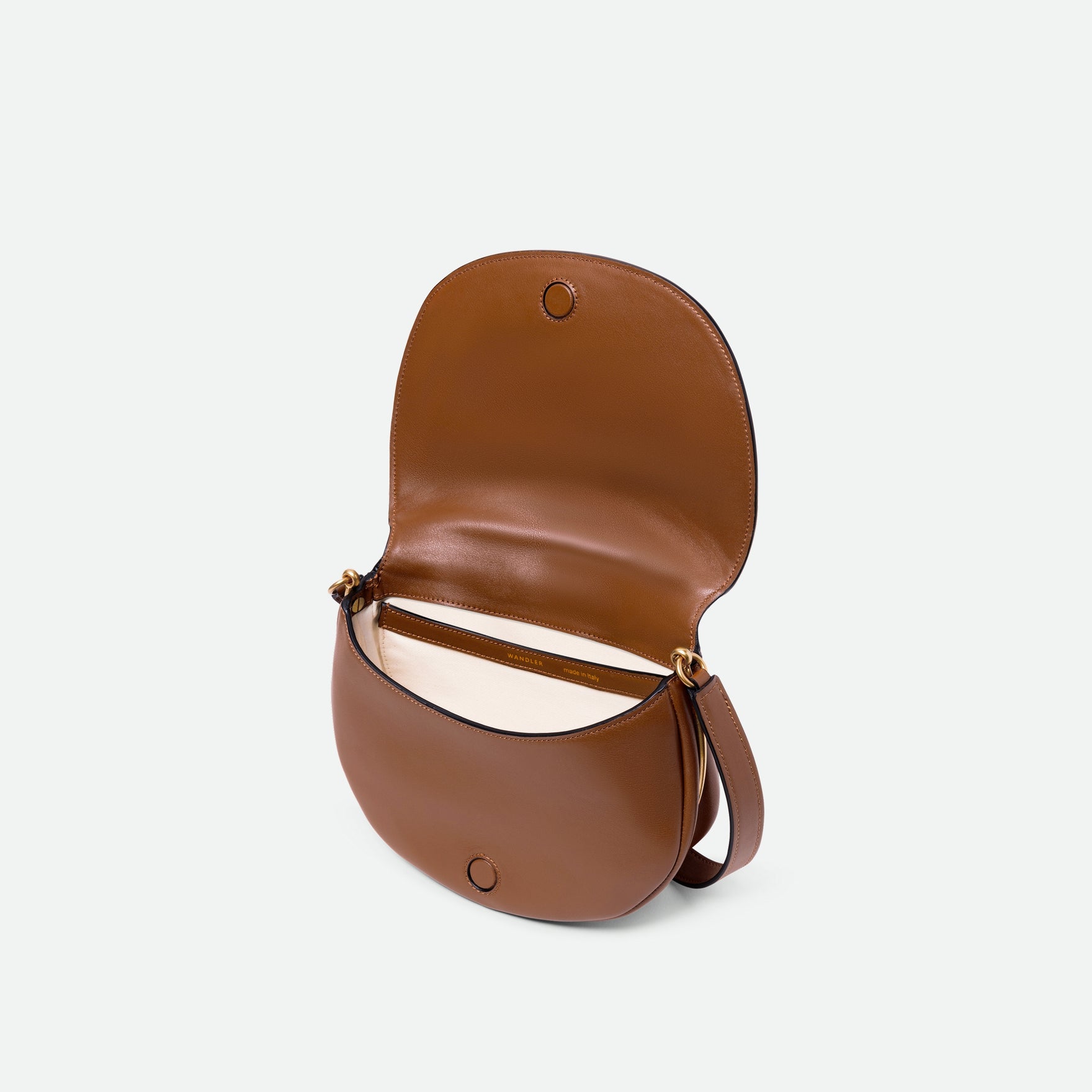 Wandler Kate Saddle Bag in Saddle, made from calf leather with golden hardware and adjustable shoulder strap, pictured with the lap of the bag open, allowing for a glimpse of the inside.