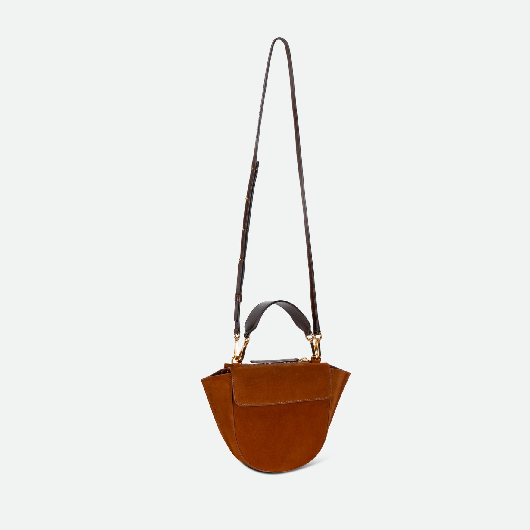 Wandler Hortensia Bag Mini in the color Tan Suede, warm brown suede, Italian calf leather with golden hardware, rounded silhouette and top handle. The bag is pictured with the crossbody strap extended into the air.