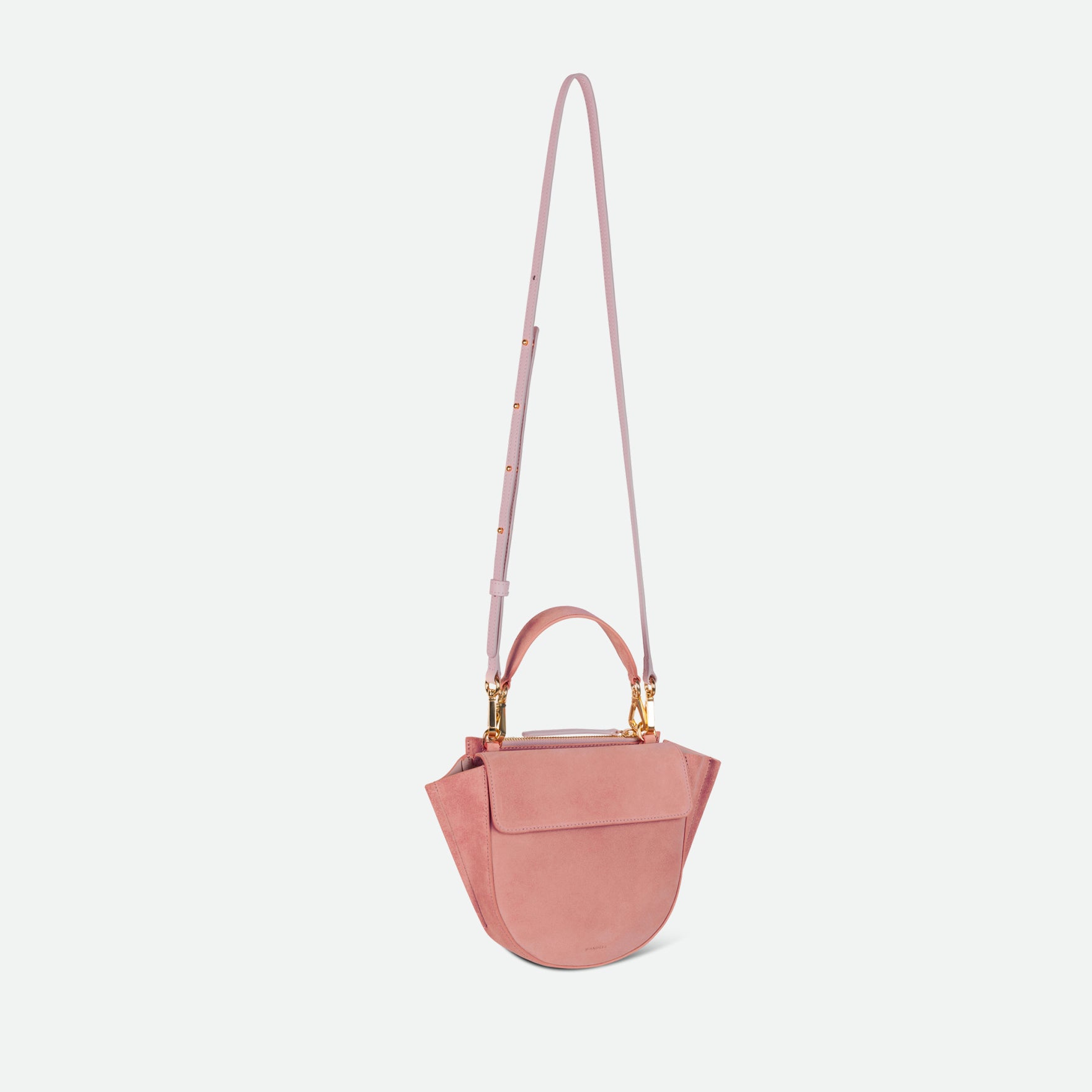 Wandler Hortensia Bag Mini in the color Apricot Suede, light pink suede, Italian calf leather with golden hardware, rounded silhouette and top handle. The bag is pictured with the crossbody strap extended into the air.