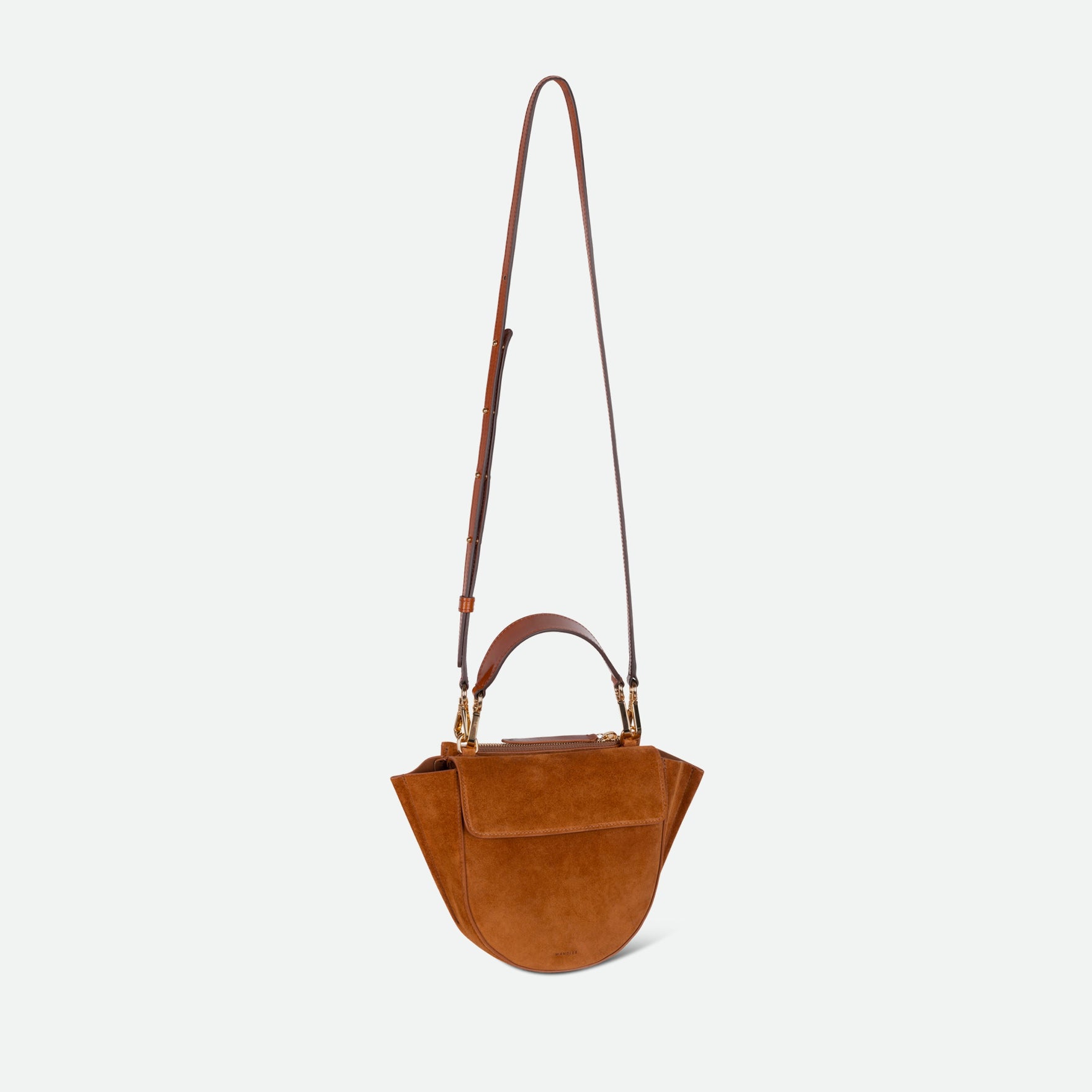 Wandler Hortensia Bag Mini in the color Cognac Suede, soft warm brown suede, Italian calf leather with golden hardware, rounded silhouette and top handle. The bag is pictured with the crossbody strap extended into the air.