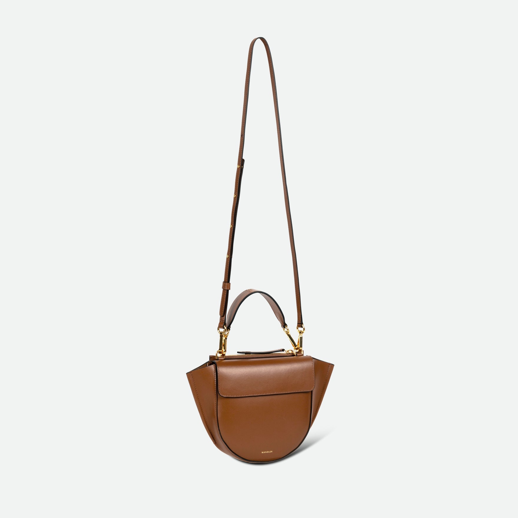 Wandler Hortensia Bag Mini in the color gingerbread, dark beige, Italian calf leather with golden hardware, rounded silhouette and top handle. The bag is pictured with the crossbody strap extended into the air.