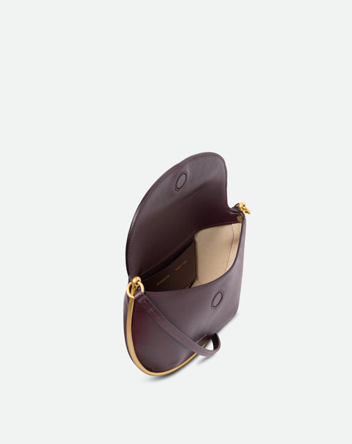 Wandler Kate Mini Crossbody in the color Grape, made from Italian calf leather with golden hardware and adjustable strap, pictured from above, allowing for a glimpse into the inside of the bag.
