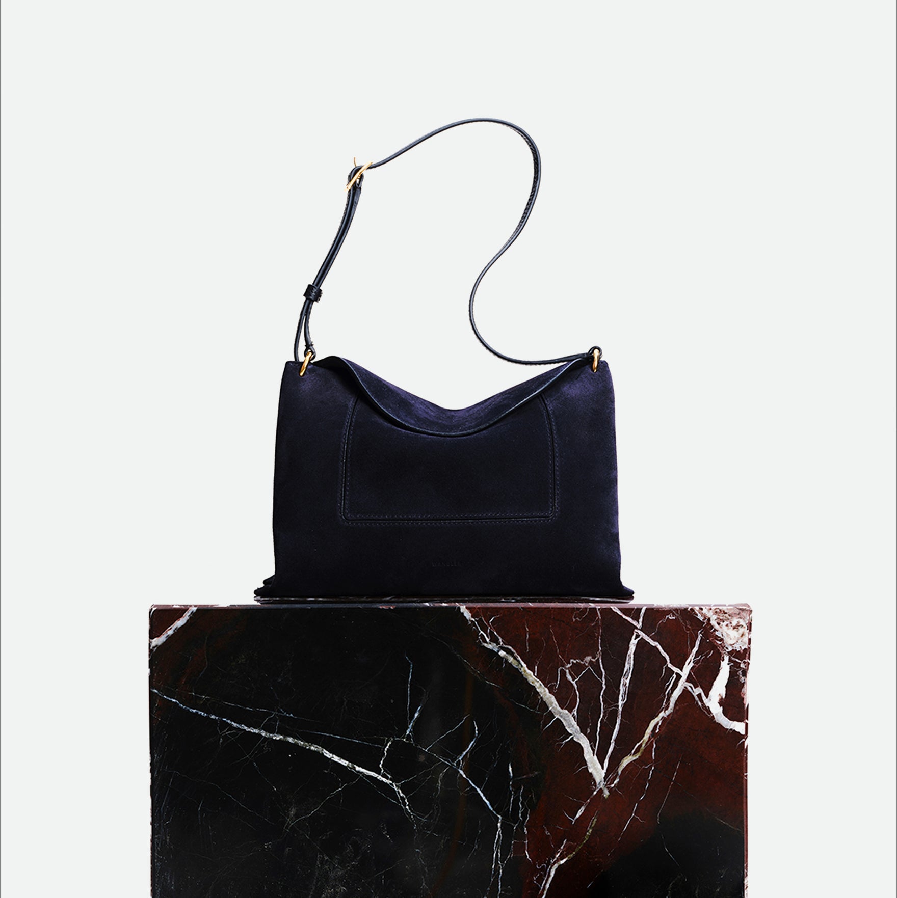 Wandler Penelope Slouch Bag in the color Orion Suede, deep dark blue, made from calf leather with golden hardware and adjustable slim strap, pictured on pillar.