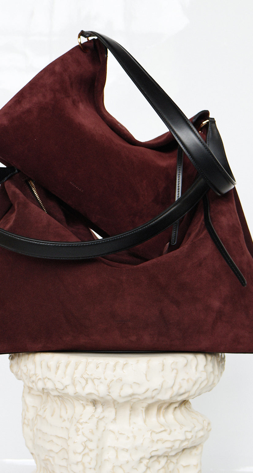 Wandler Penelope Tote Small in the color Acai Suede / Black made from calf leather with golden hardware and soft slouchy silhouette, pictured on pillar together with the regular Penelope Tote Acai Suede / Black to show the difference in size.