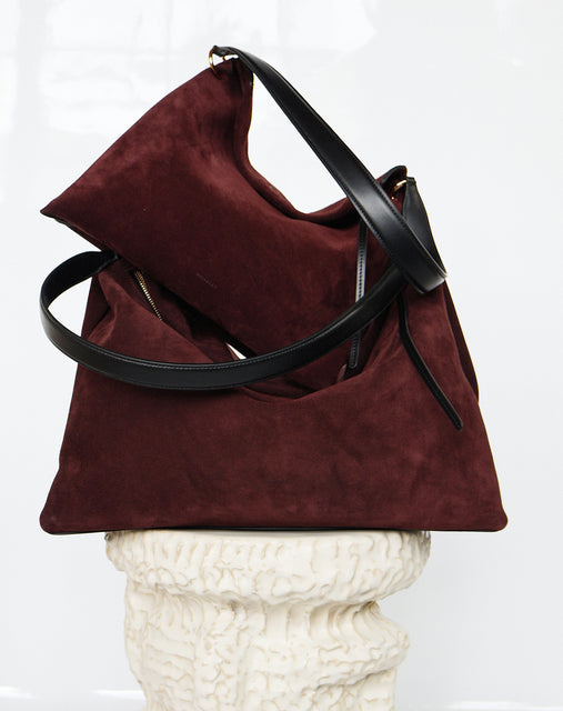 Wandler Penelope Tote Small in the color Acai Suede / Black made from calf leather with golden hardware and soft slouchy silhouette, pictured on pillar together with the regular Penelope Tote Acai Suede / Black to show the difference in size.