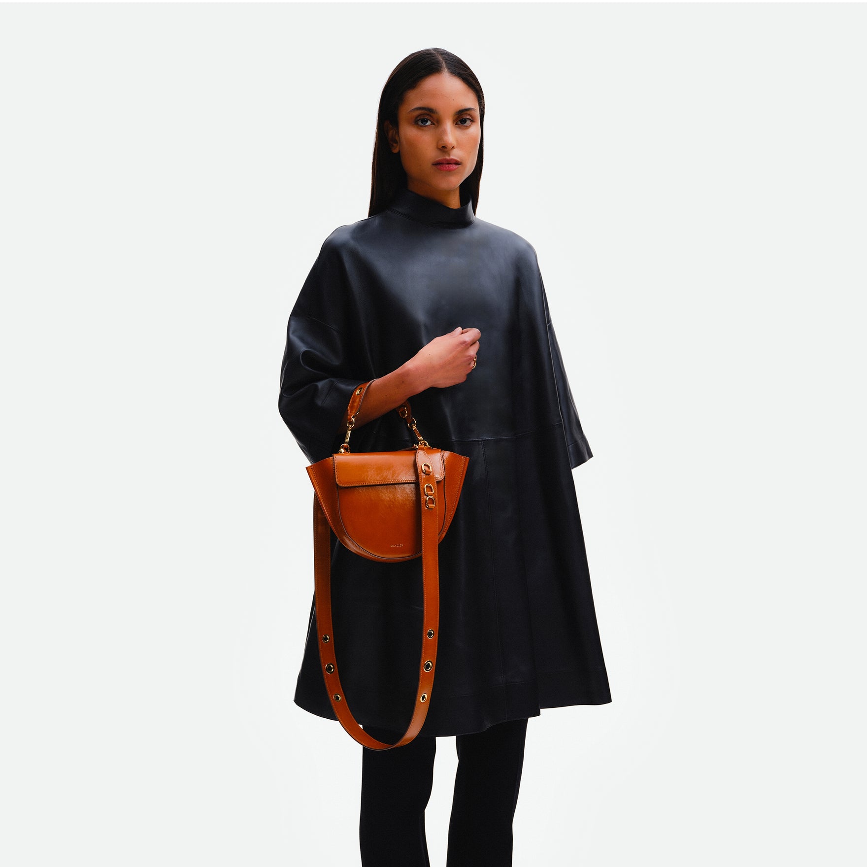 Wandler Hortensia Bag Mini in the color Cognac Eyelets, caramel brown, Italian calf leather with golden hardware, rounded silhouette and top handle, pictured being held on the forearm by model. 